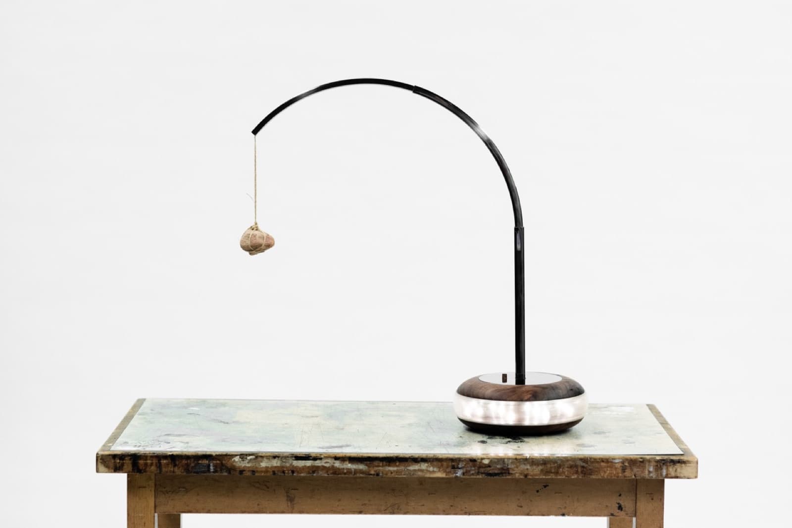 A desk lamp with a curved black arm and a wrapped stone hanging from its tip over a wood-and-steel base