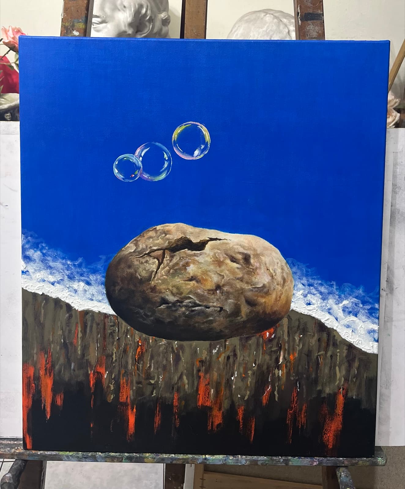 Acrylic painting of a cracked stone floating over a fiery horizon under three bubbles, on an easel